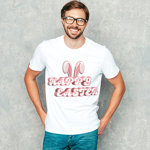Smiling man wearing white T-shirt featuring pink “Happy Easter” text with bunny ears, standing against light grey studio wall.