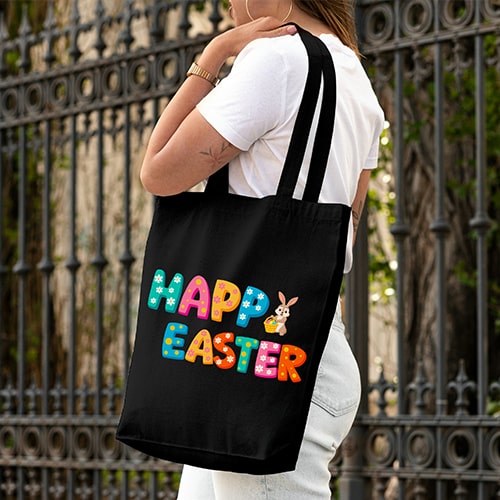Person carrying a black tote bag with colorful Happy Easter text and a cute bunny illustration for festive celebrations.